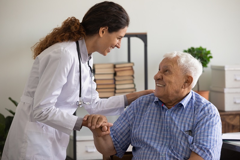 An elderly patient holds hands with a young doctor