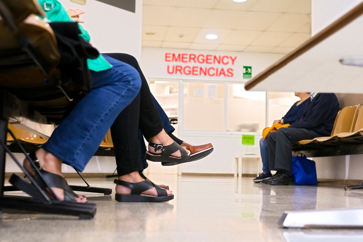 Four people sit in chairs facing each other in front of a sign with text that reads Emergency Urgencias