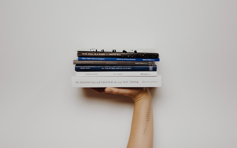 Hand holding four books stacked on top of each other. 