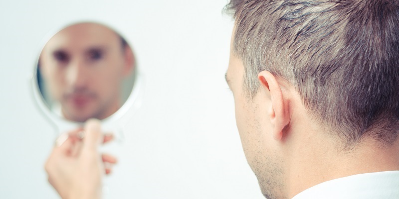 A clean shaven man looks into a small hand mirror