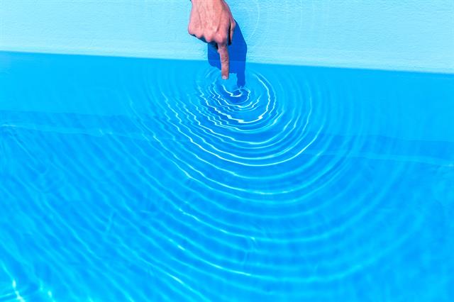 A finger dips into a bright blue pool causing circular ripples