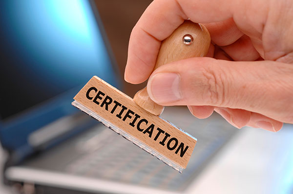 A hand holds a wooden stamp that says certification