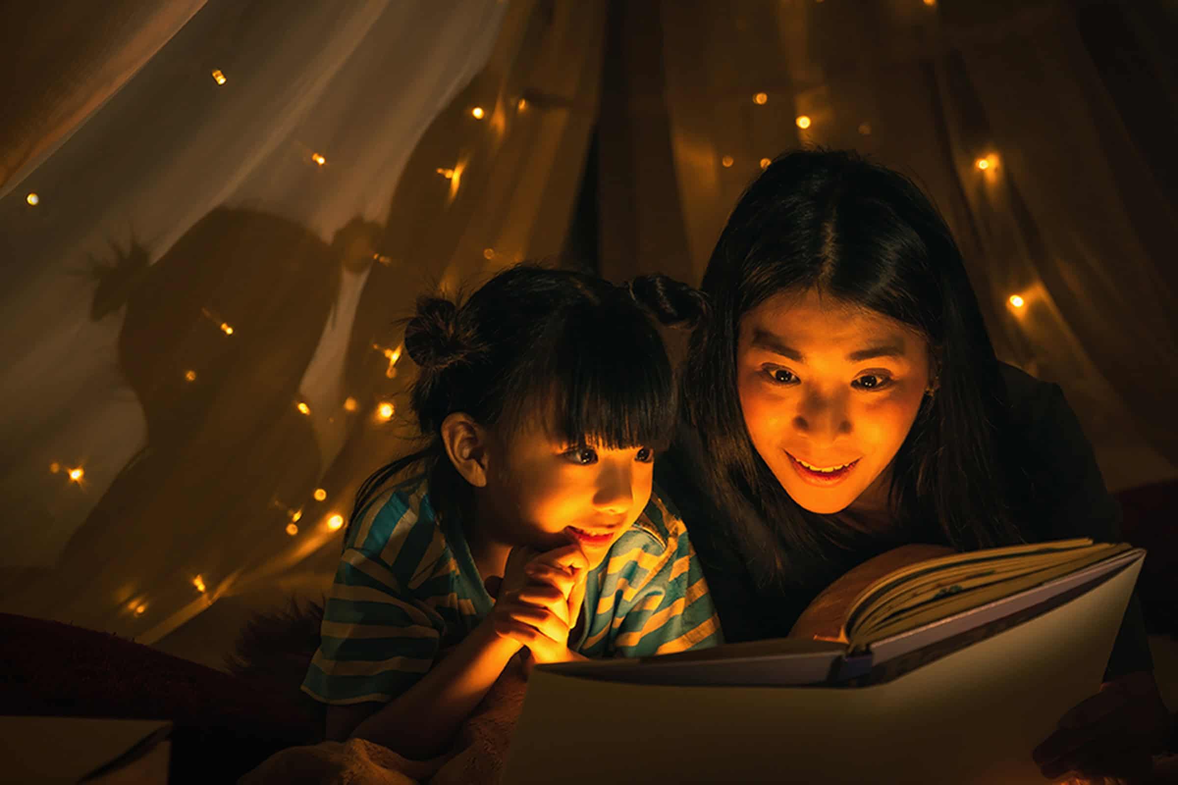A mother reading her daughter a bedtime story in a tent