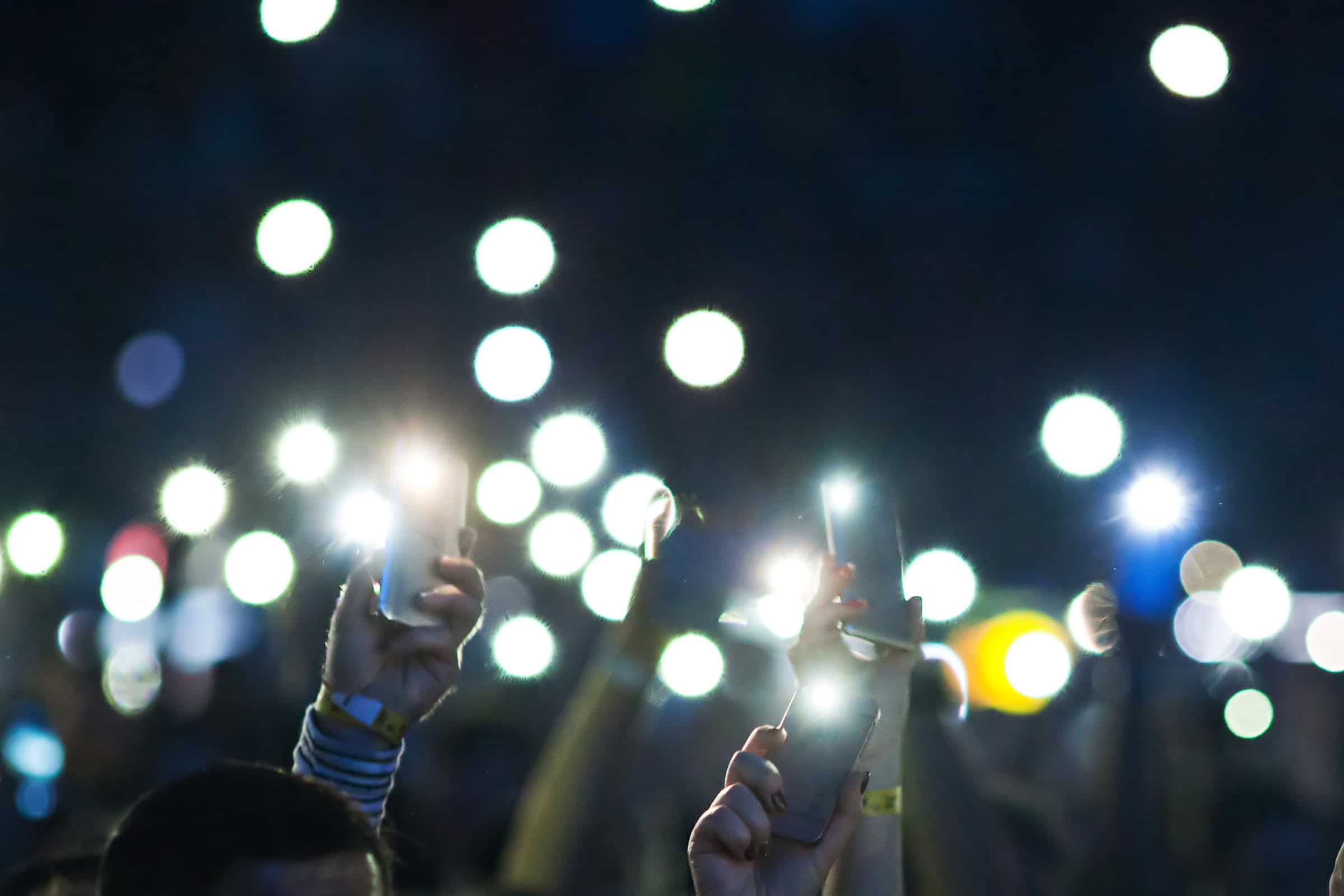 Hands raising their phone flashlights at a concert