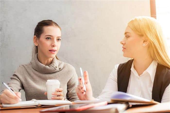 Two women writing and having a conversation