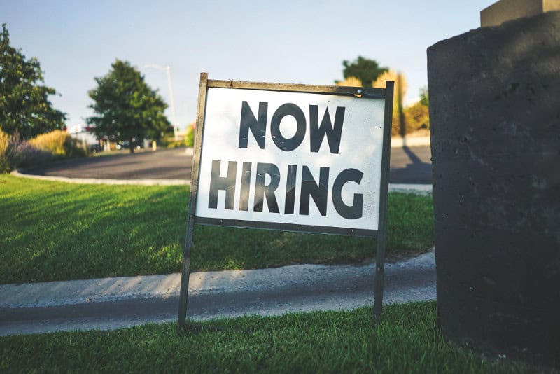 A sign that says "now hiring" on a lawn
