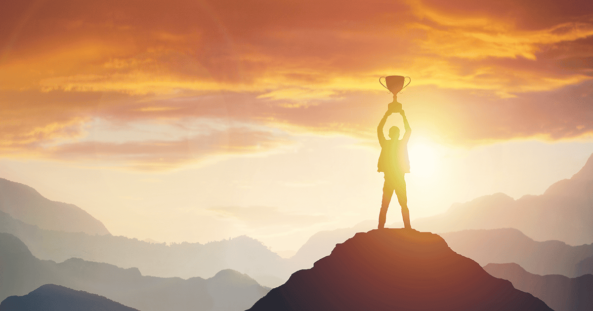 A person raising a trophy on a mountaintop
