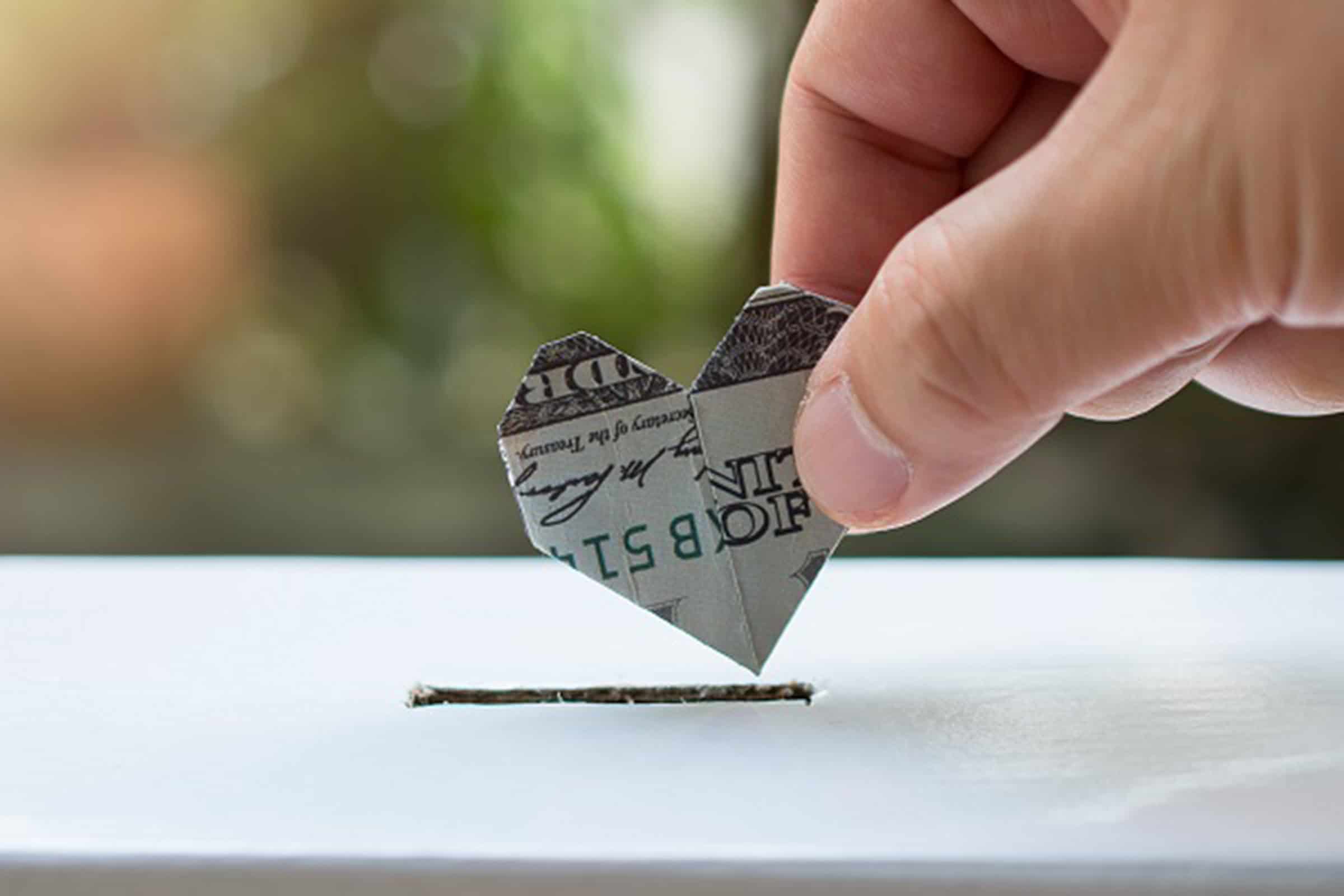 A hand putting a folded dollar into a box